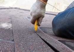 Denver roofing worker cuts shingles on the roof.